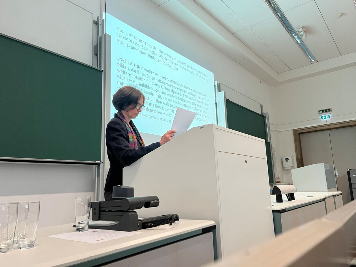 Philine Lautenschläger steht an einem Pult und trägt vor. Im Hintergrund ist ihre Präsentation zu sehen.